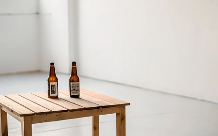 Формирование алкоголизма Две бутылки пива на деревянном столе в пустой белой комнате
